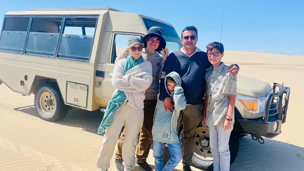Eine Familie steht vor einem großen Safari-Jeep in der Wüste