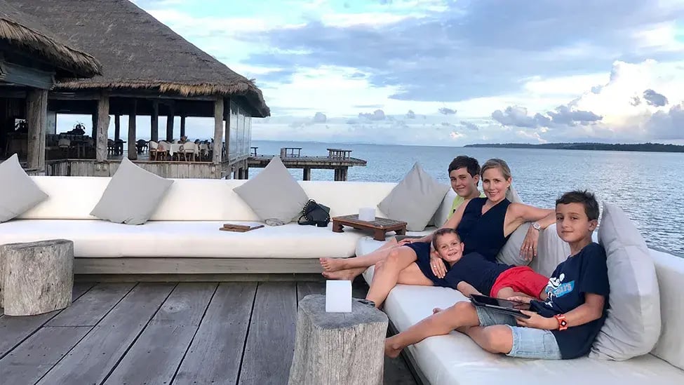 Eine Mutter sitzt mit ihren drei Söhnen auf einer gemütlichen Sitzlounge mit Aussicht aufs Meer