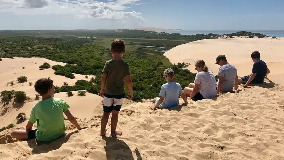 Sechs Kinder sitzen auf dem Rand einer Düne