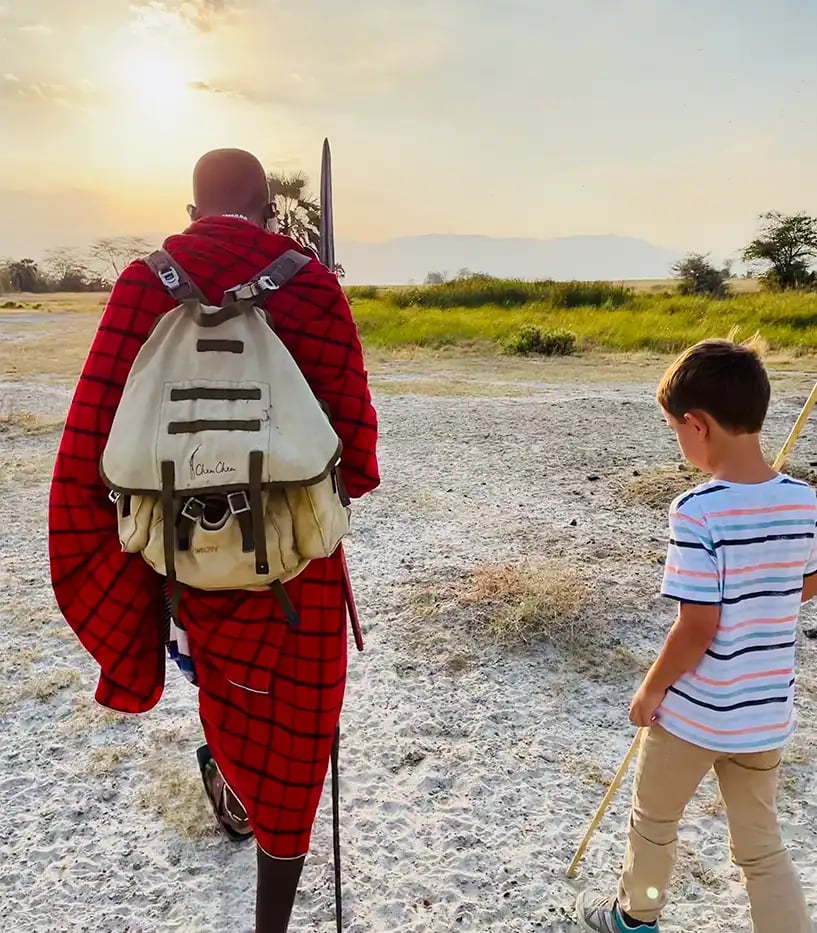Ein kleiner Junge und ein afrikanischer Einwohner sind von hinten zu sehen, während sie durch die Steppe gehen.