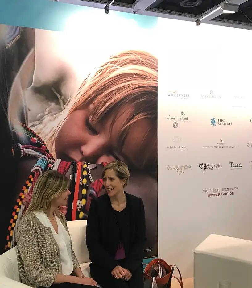 Zwei Frauen sitzen vor einer Messewand mit einem Kinderfoto und unterhalten sich