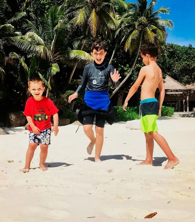 Drei Jungen in Badebekleidung posieren an einem Sandstrand mit Palmen vor der Kamera