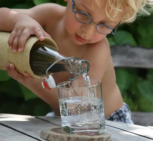Ein blonder Junge mit Brille schenkt Wasser aus einer Wasserflasche in ein Glas