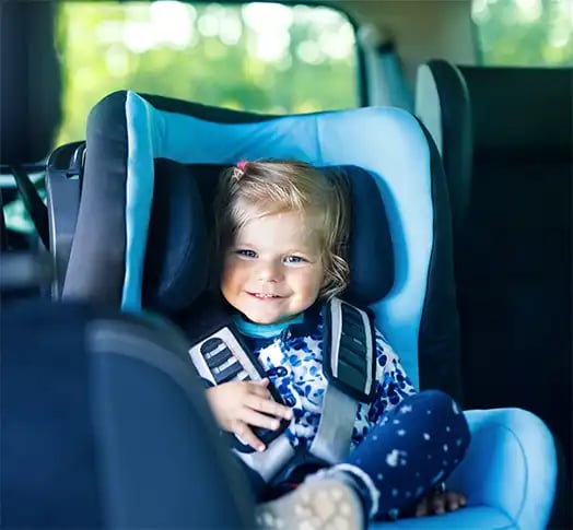 Ein kleines Mädchen sitzt lächelnd in einem Kindersitz im Auto