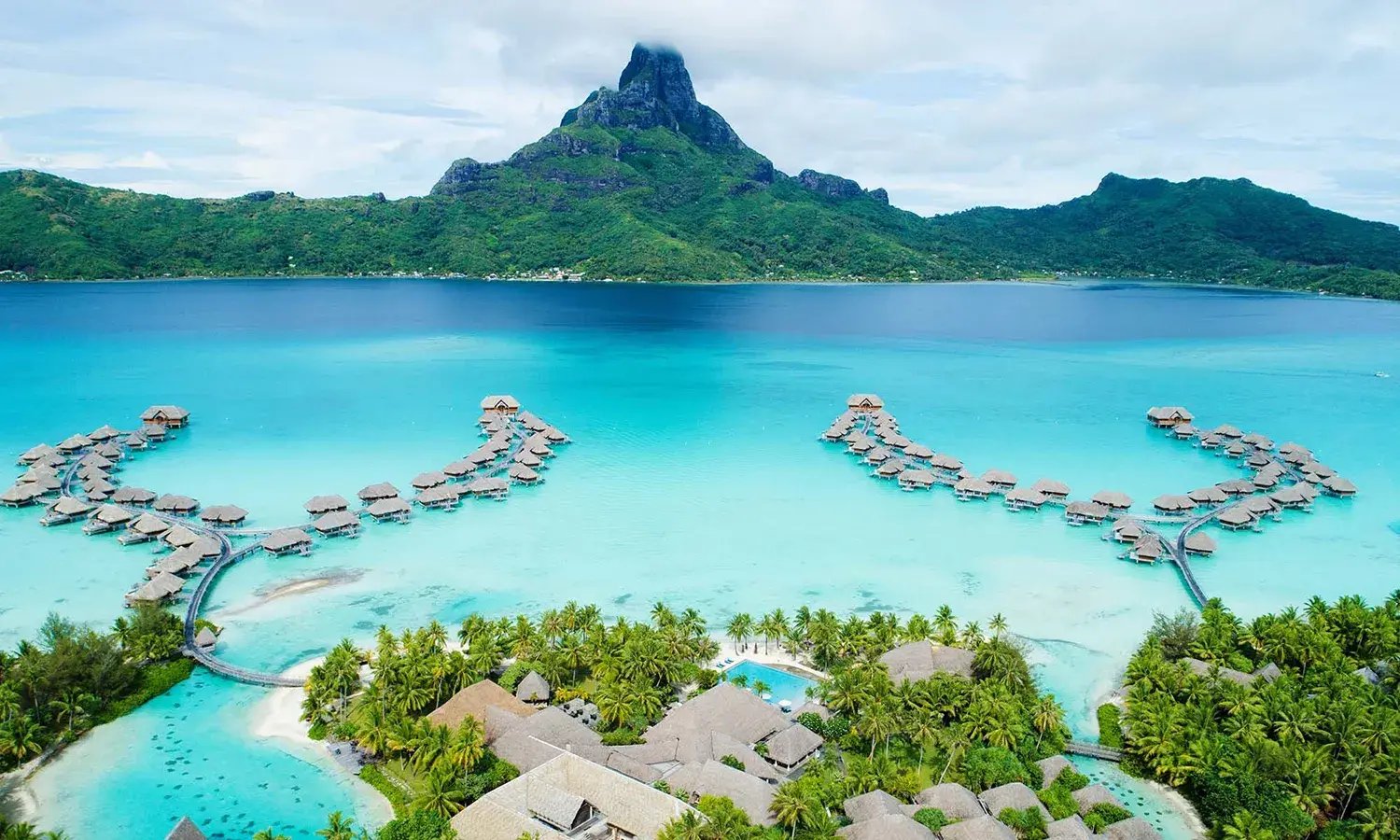 Overwater Villen im Hellblauen Wasser, im Hinergrund eine grüne Landschaft