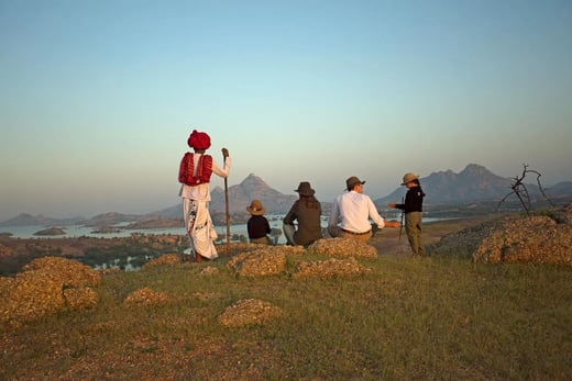Eine Familie mit zwei Kindern und ein Einheimischer in traditioneller Kleidung von hinten fotografiert, blicken auf die Landschaft 