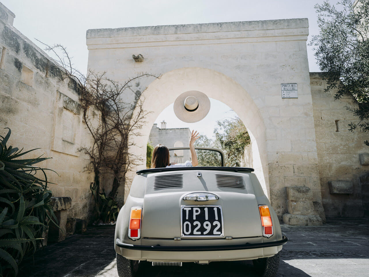 Eine Frau fährt mit einem Oldtimer durch die Pforte von Borgo Egnazia, Apulien.