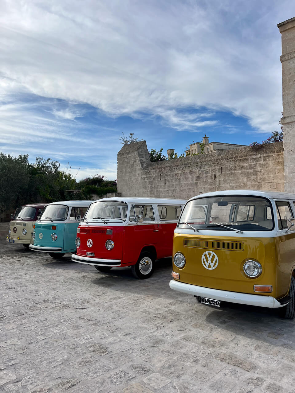 Bunte VW-Bullis reihen sich vor den Mauern Borgo Egnazias, Apulien, nebeneinander.