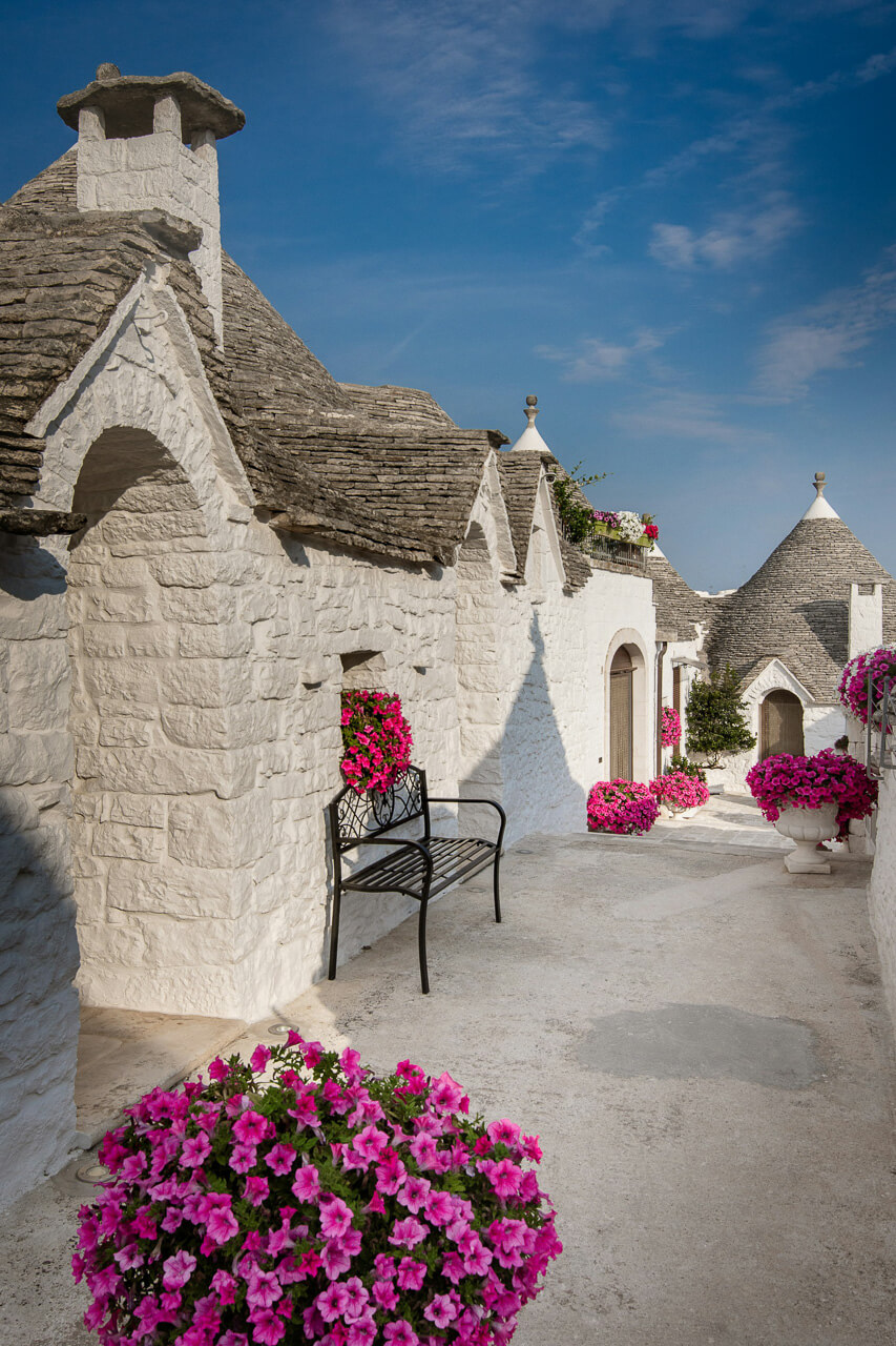 Gasse mit weißen Trulli und pinkem Blumendekor in Alberobello.