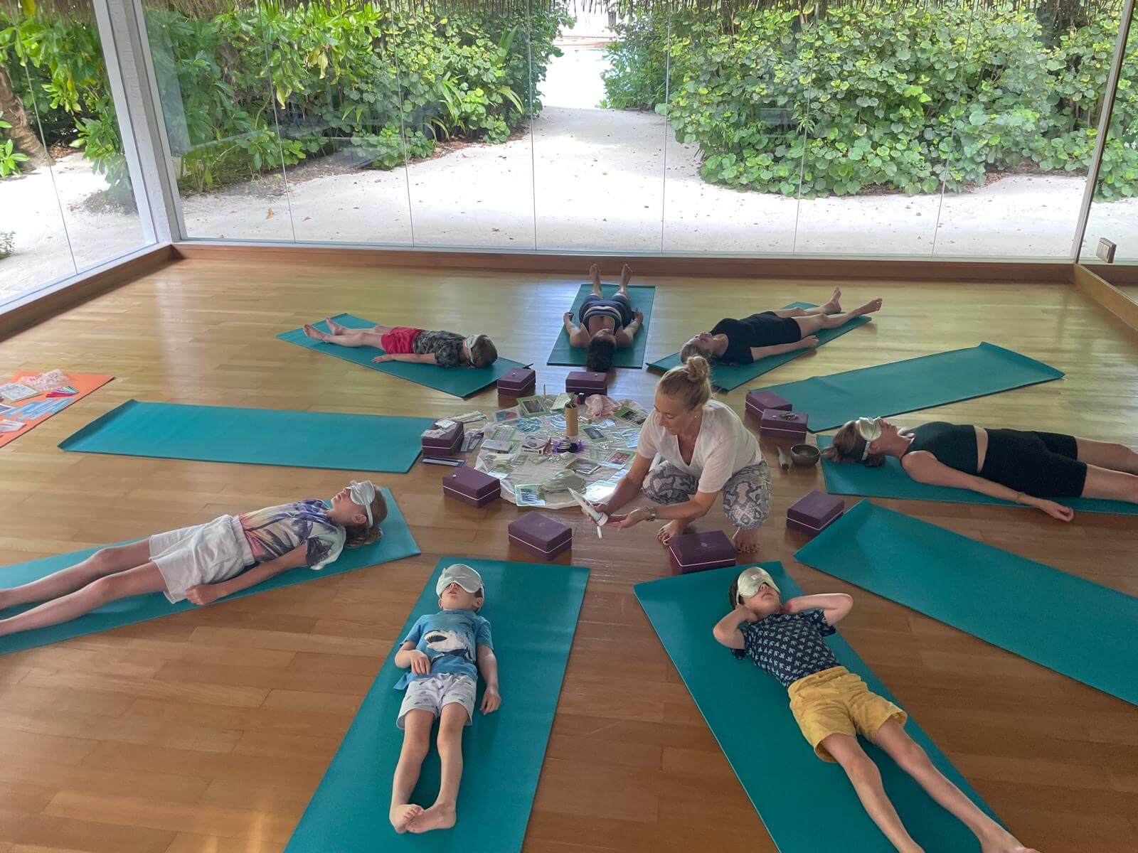 Sieben Kinder liegen mit Augenmaske für eine Entspannungsübung auf Yogamatten.