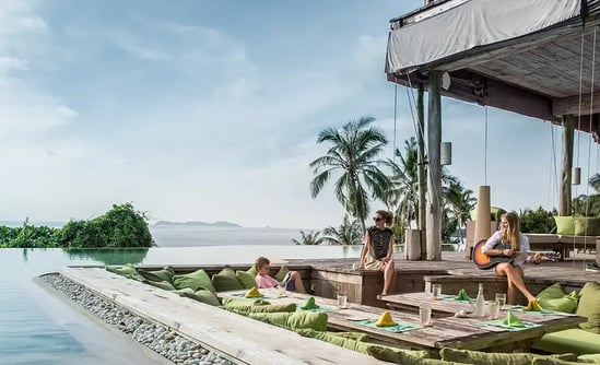 Drei Frauen sitzen auf verschiedenen Sitzgelegenheiten an einem Infinitypool 