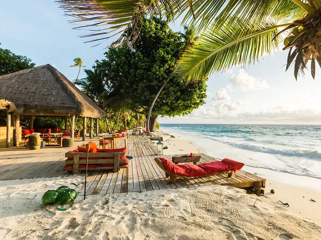 Ein traumhafter Strand am Meer auf den Seychellen mit gemütlichen Liegen und Palmen.