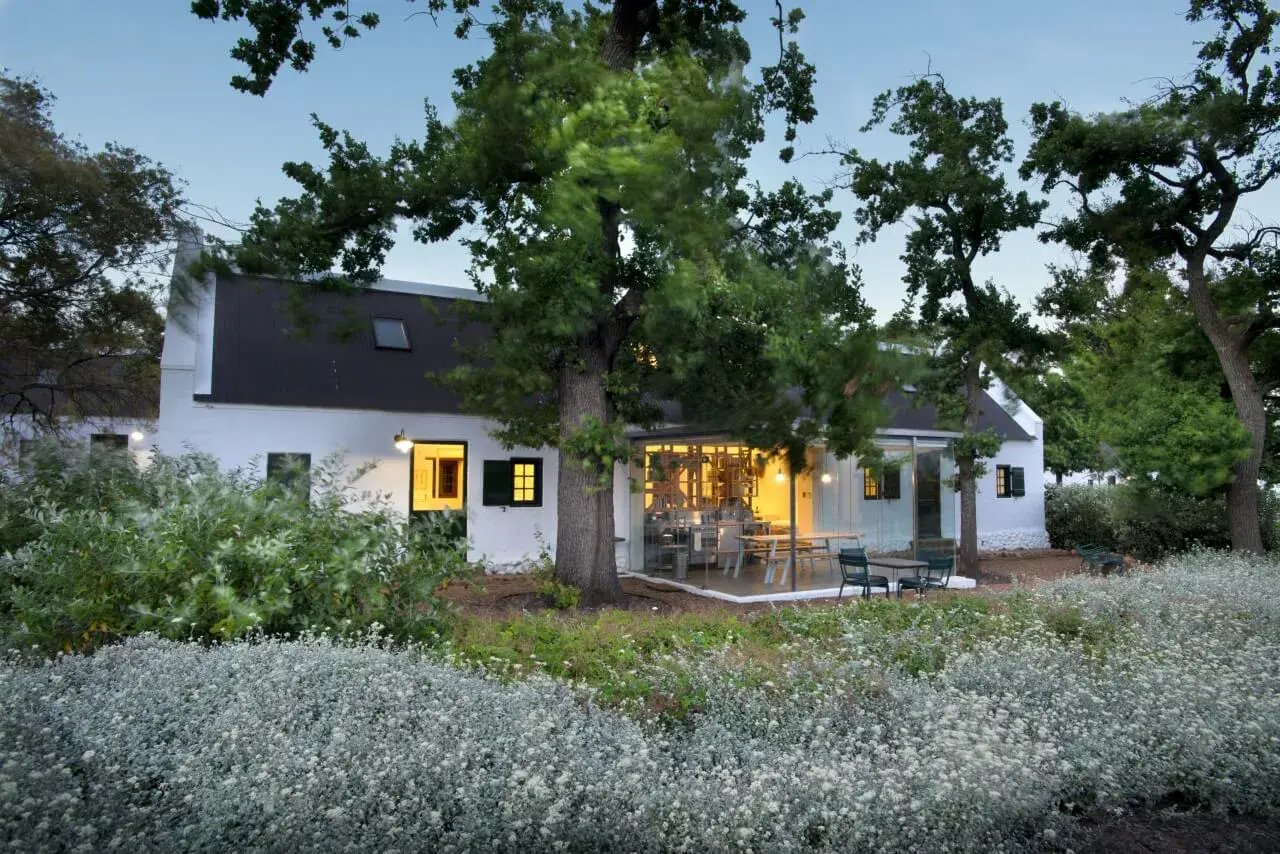 Beleuchtetes Gartenhaus mit großem Baum davor.