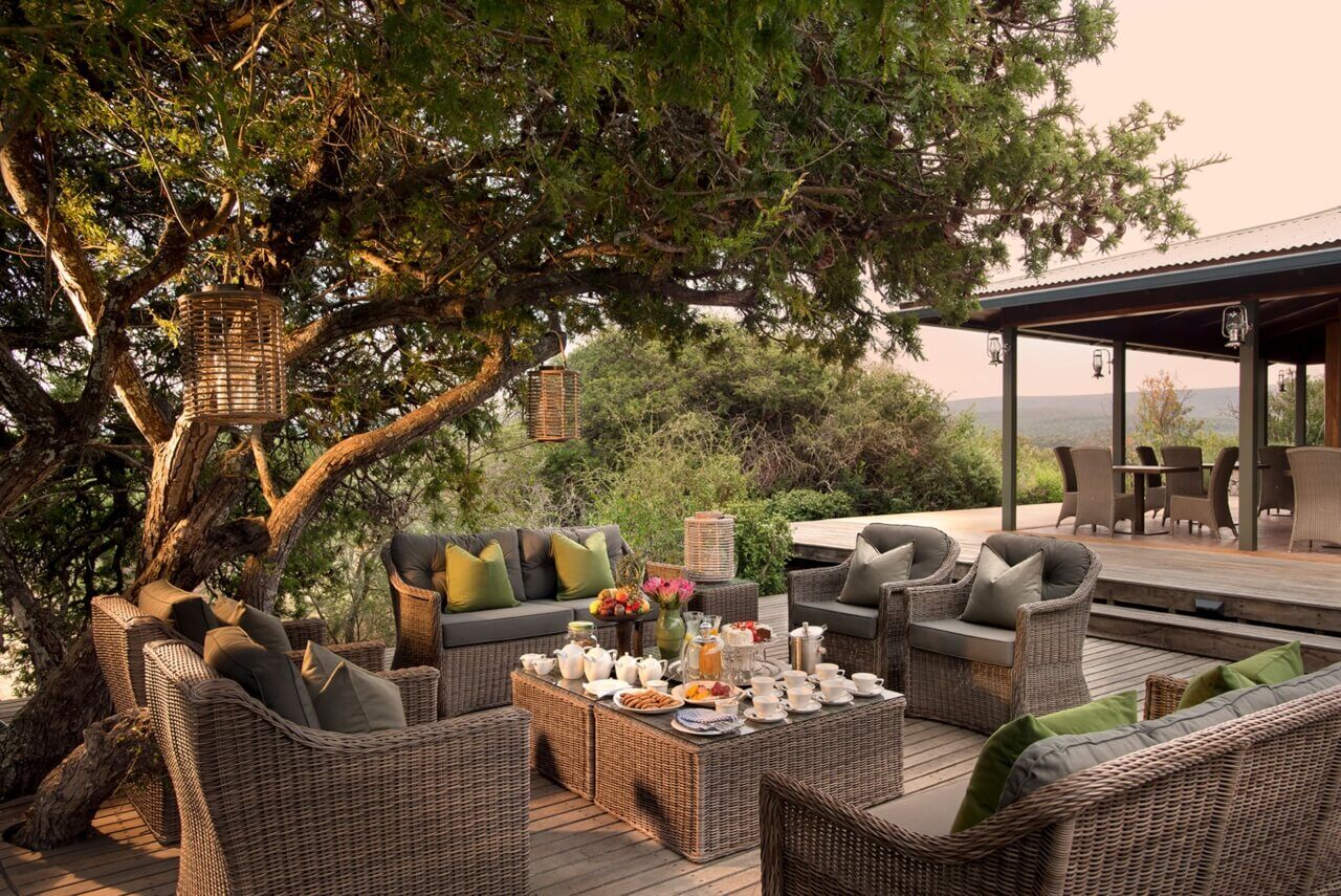 Gemütliche Sitzmöbel aus Rattan auf einer Terrasse unter einem großen Baum.