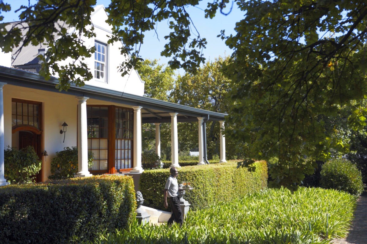 Ein Butler kommt aus einem Haus in den Garten und serviert Getränke.