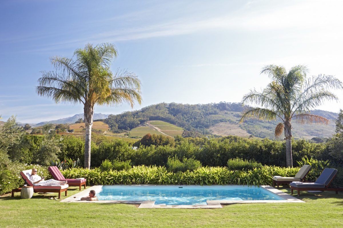 Pool mit Liegen und Palmen vor der üppigen Hügellandschaft Südafrikas.