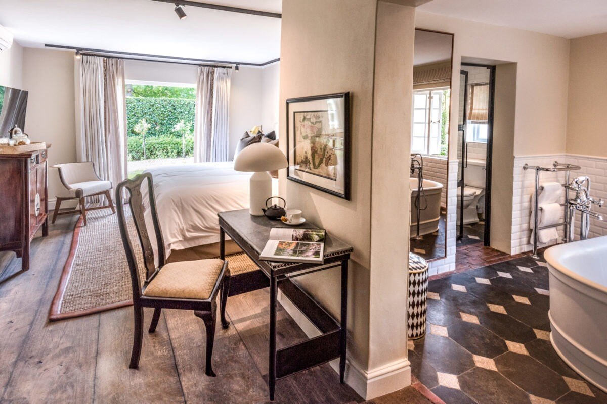 Cremefarbene Inneneinrichtung einer Suite, mit Schreibtisch, Badezimmer und Blick in den Garten.