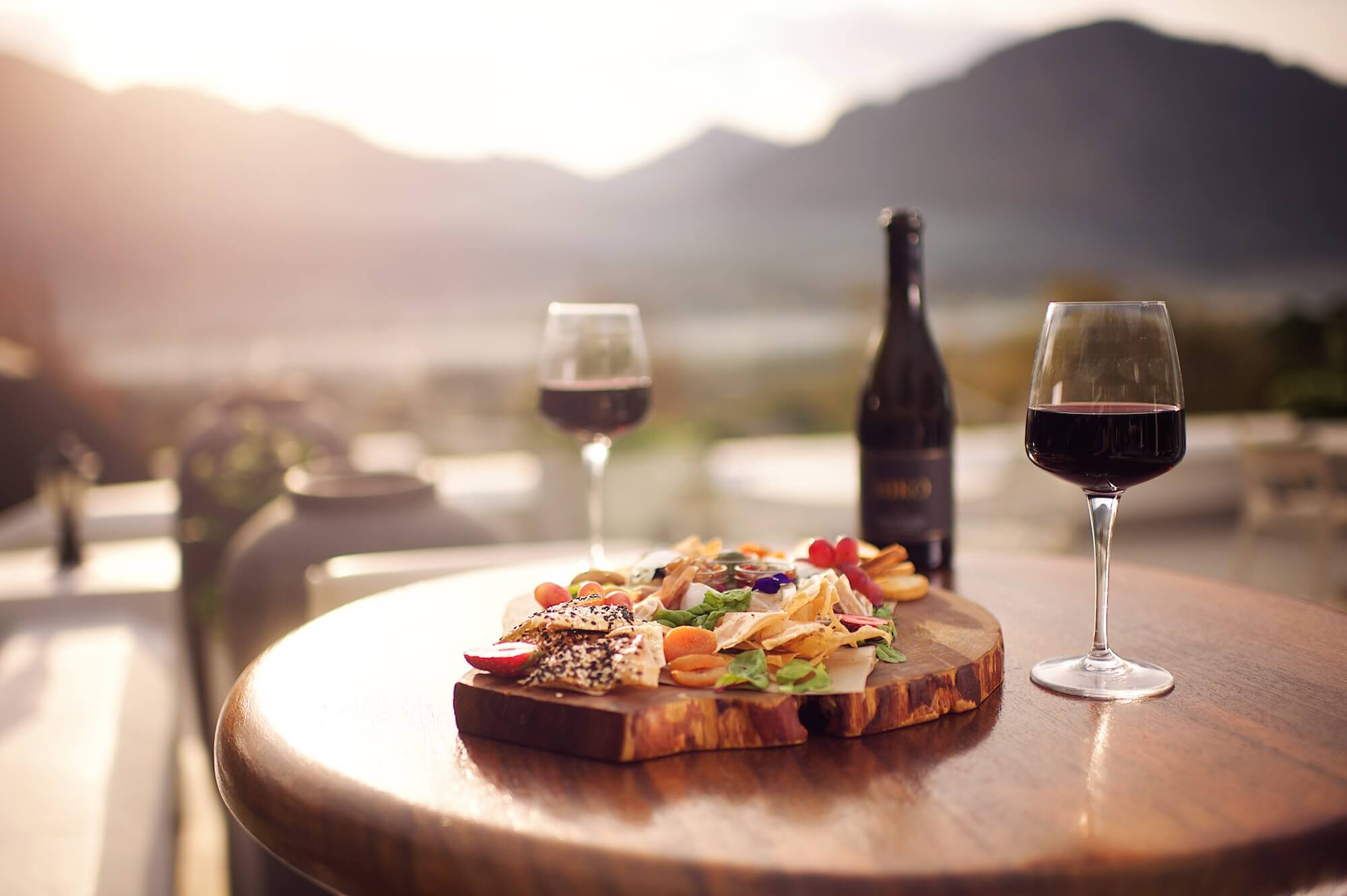 Auf einem Tisch auf einer Terrasse stehen eine Flasche Rotwein und eine Platte mit frischen Snacks.