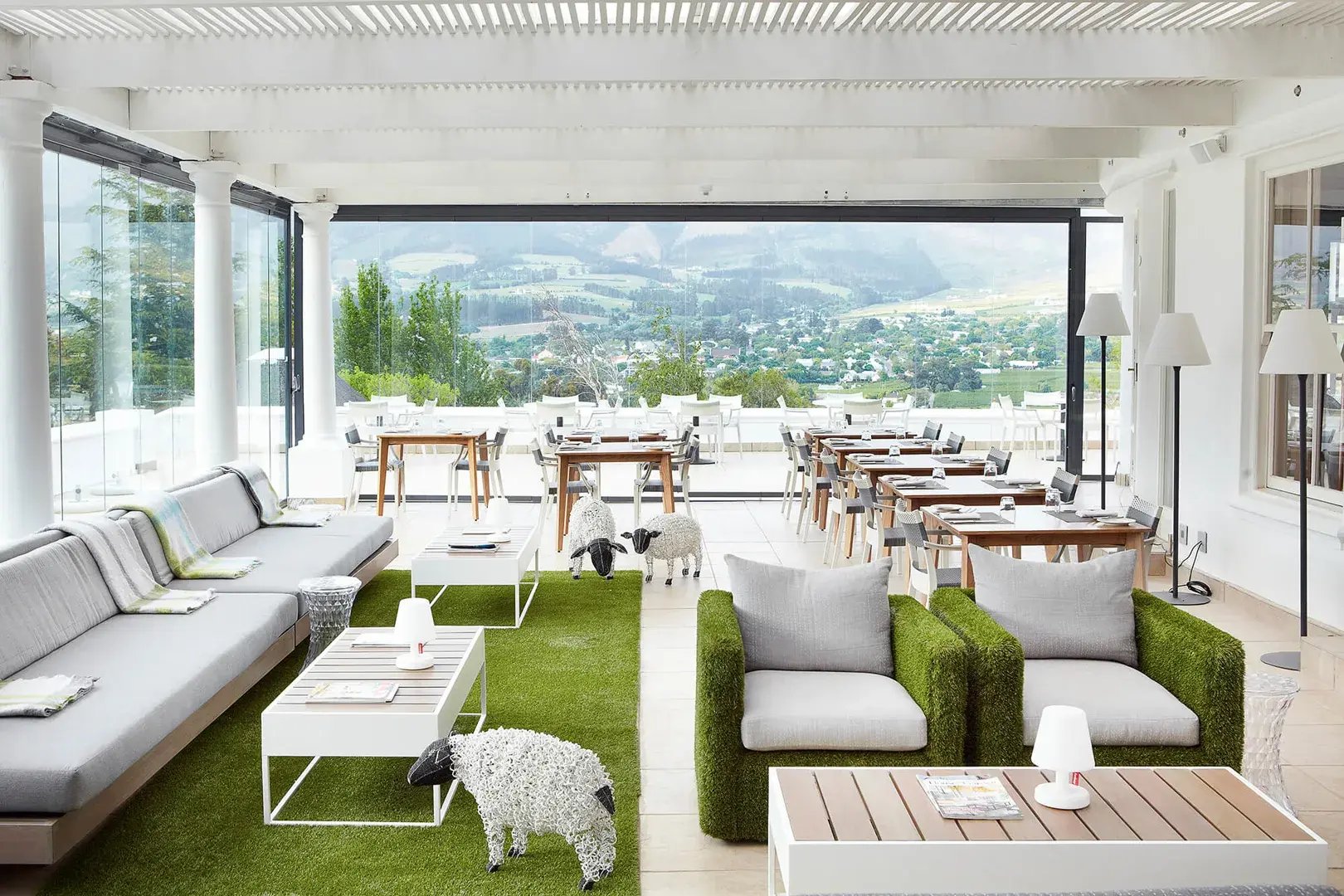 Helle Restaurantterrasse mit weißen Möbeln und grünem Boden.