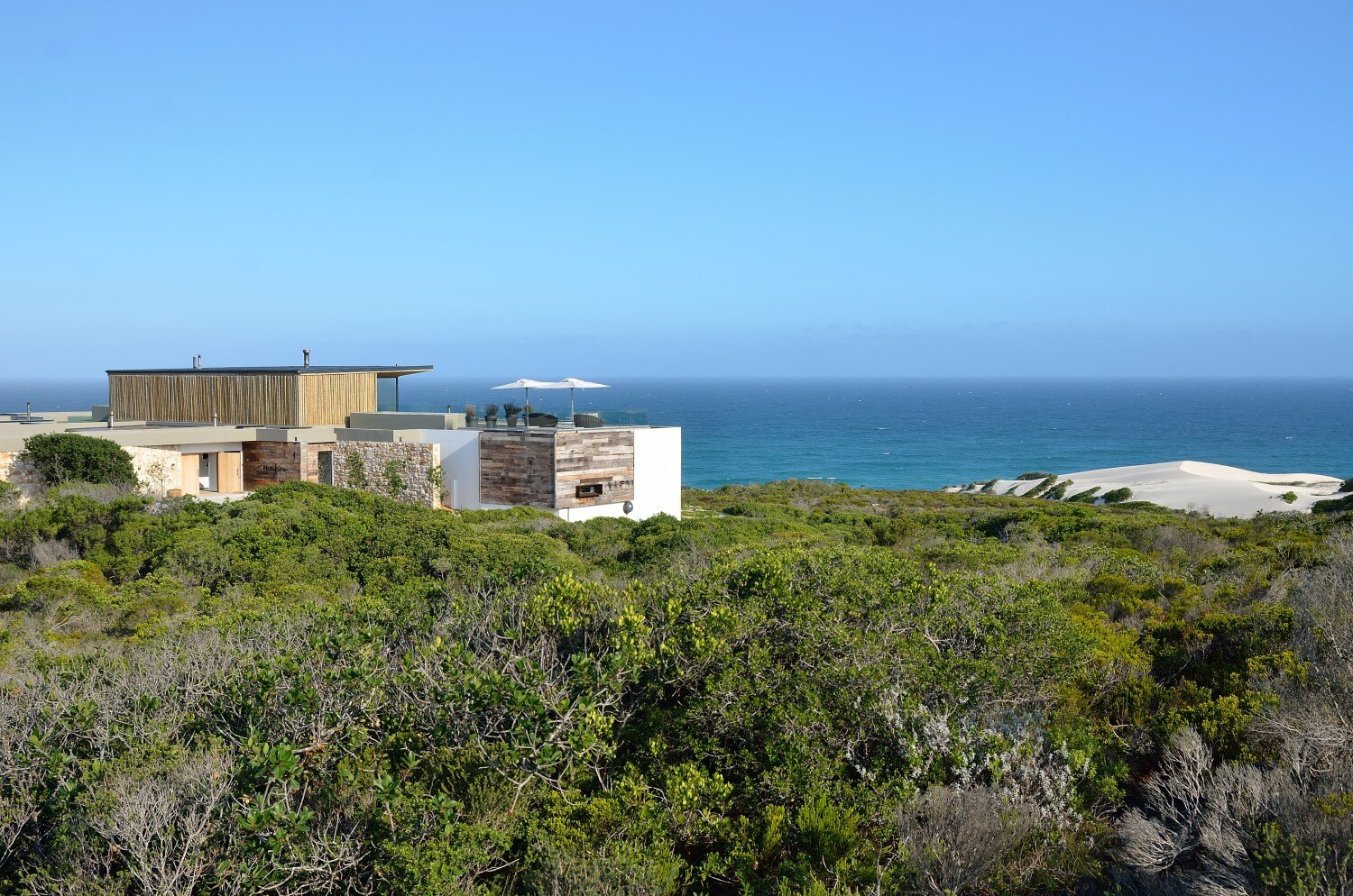 Außenansicht einer Beach Lodge, die in grüner Vegetation mit Blick auf den Ozean steht.
