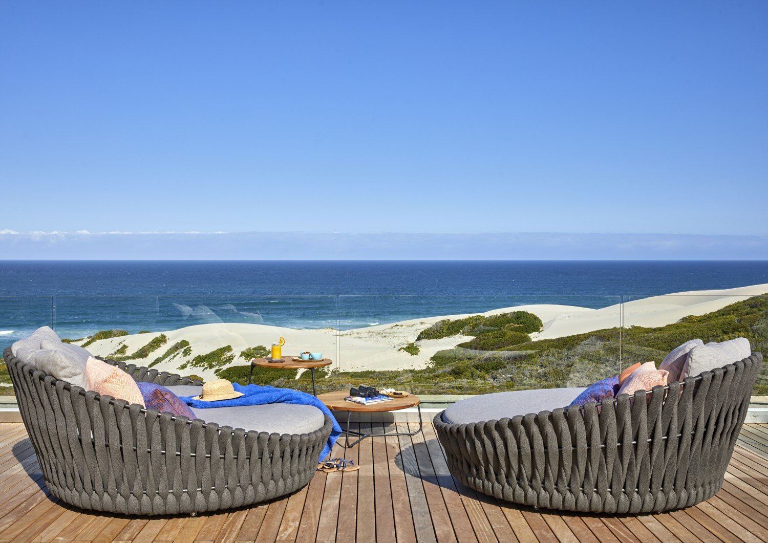 Zwei Korbsessel stehen auf einer Holzterrasse mit Blick aufs Meer.