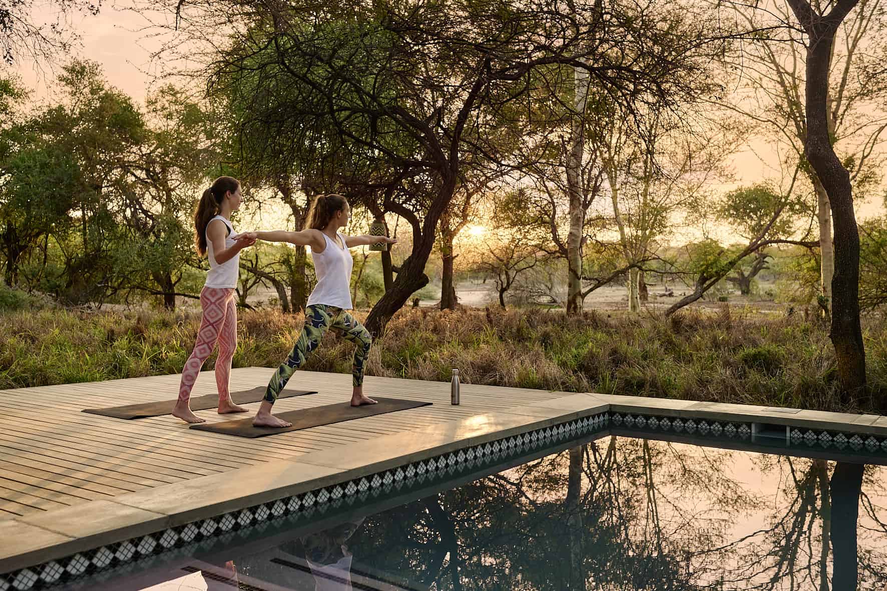 Zwei Frauen machen Yoga neben einem Pool.