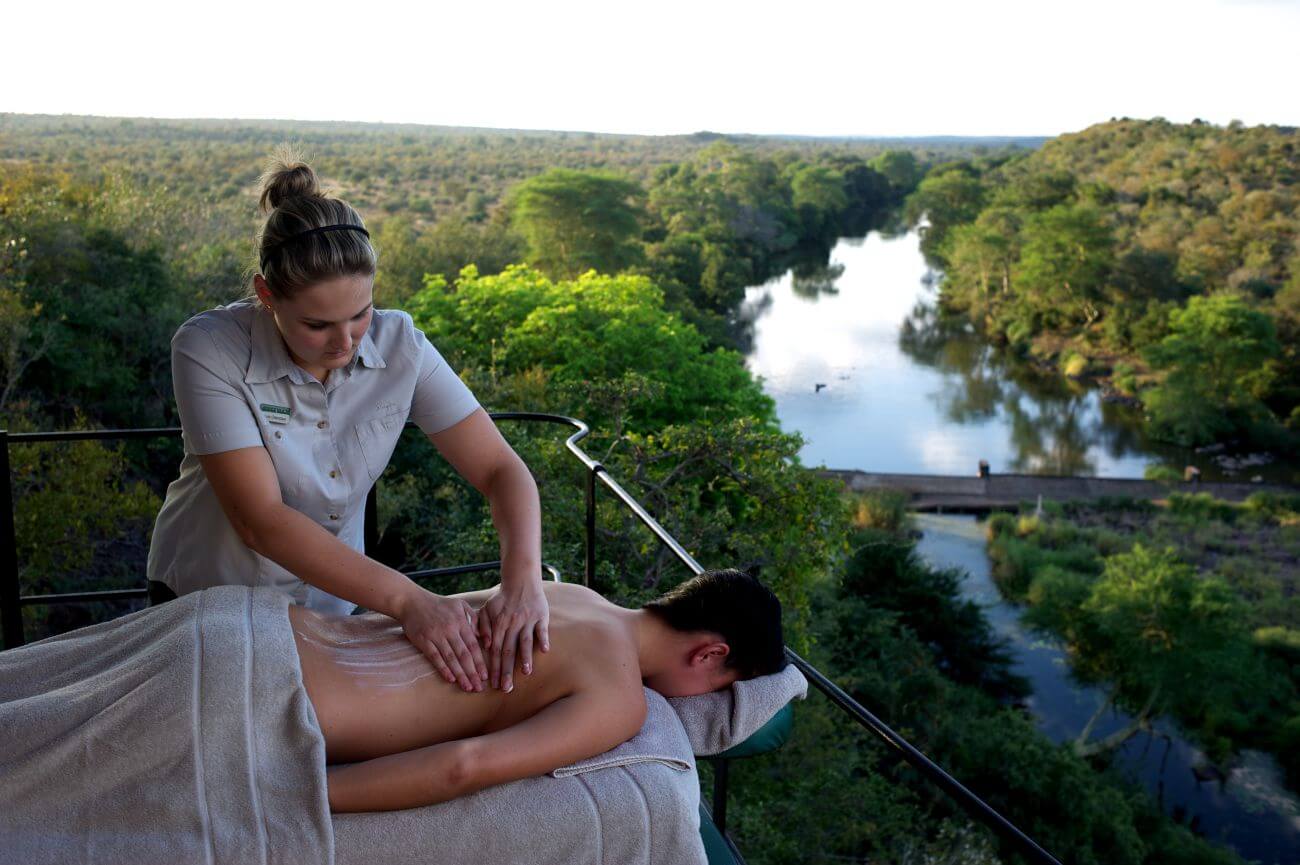 Ein Mann erhält eine Massage auf einer Terrasse, im Hintergrund fließt ein Fluss.