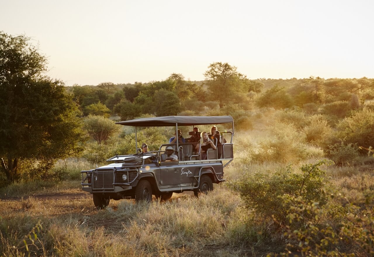 Safarijeep fährt bei Sonnenaufgang durch den Busch.