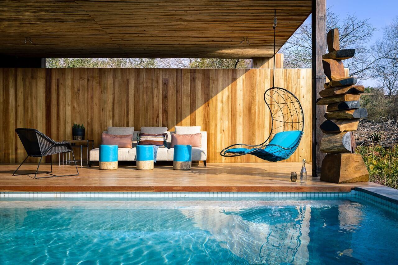 Swimmingpool mit Terrasse, auf der sich eine Liegeschaukel befindet.