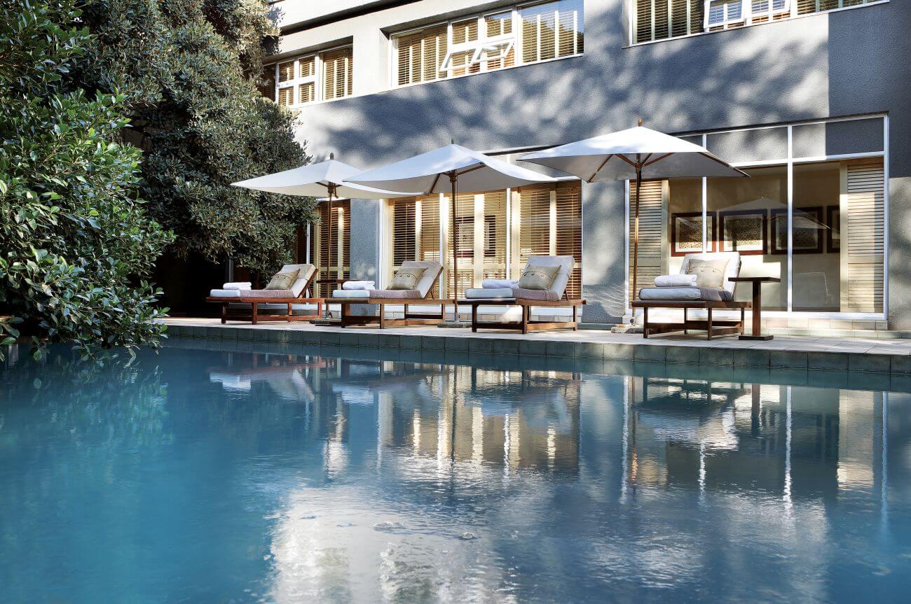 Großer Pool vor einem Hotel, am Poolrand sind Liegen und Sonnenschirme.