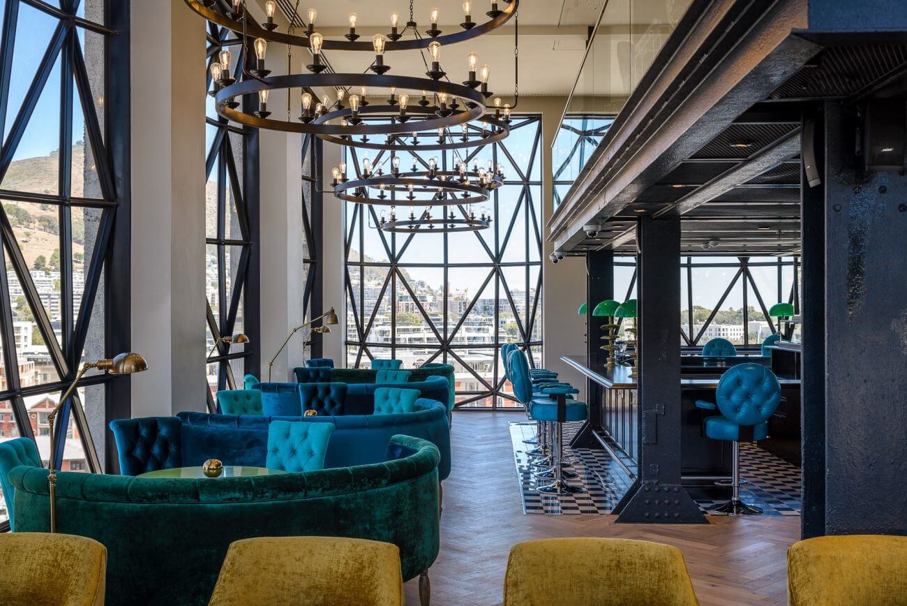 Hotellounge mit Kronleuchtern und türkisen und gelben samtbezogenen Sitzmöbeln.