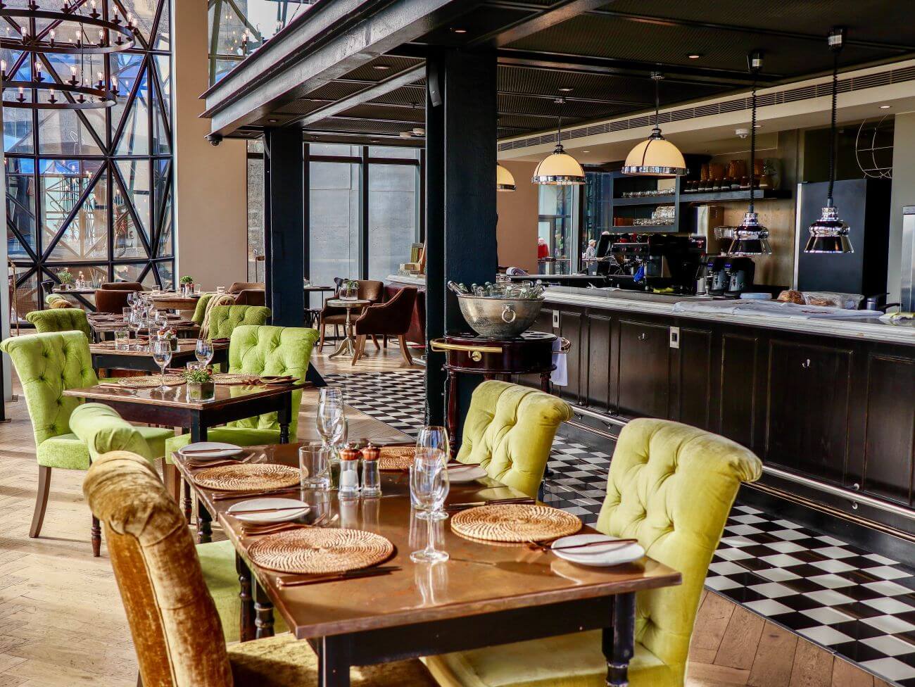 Speisezimmer mit grünen Stühlen und gedecktem Tisch. Im Hintergrund ist eine Bar.
