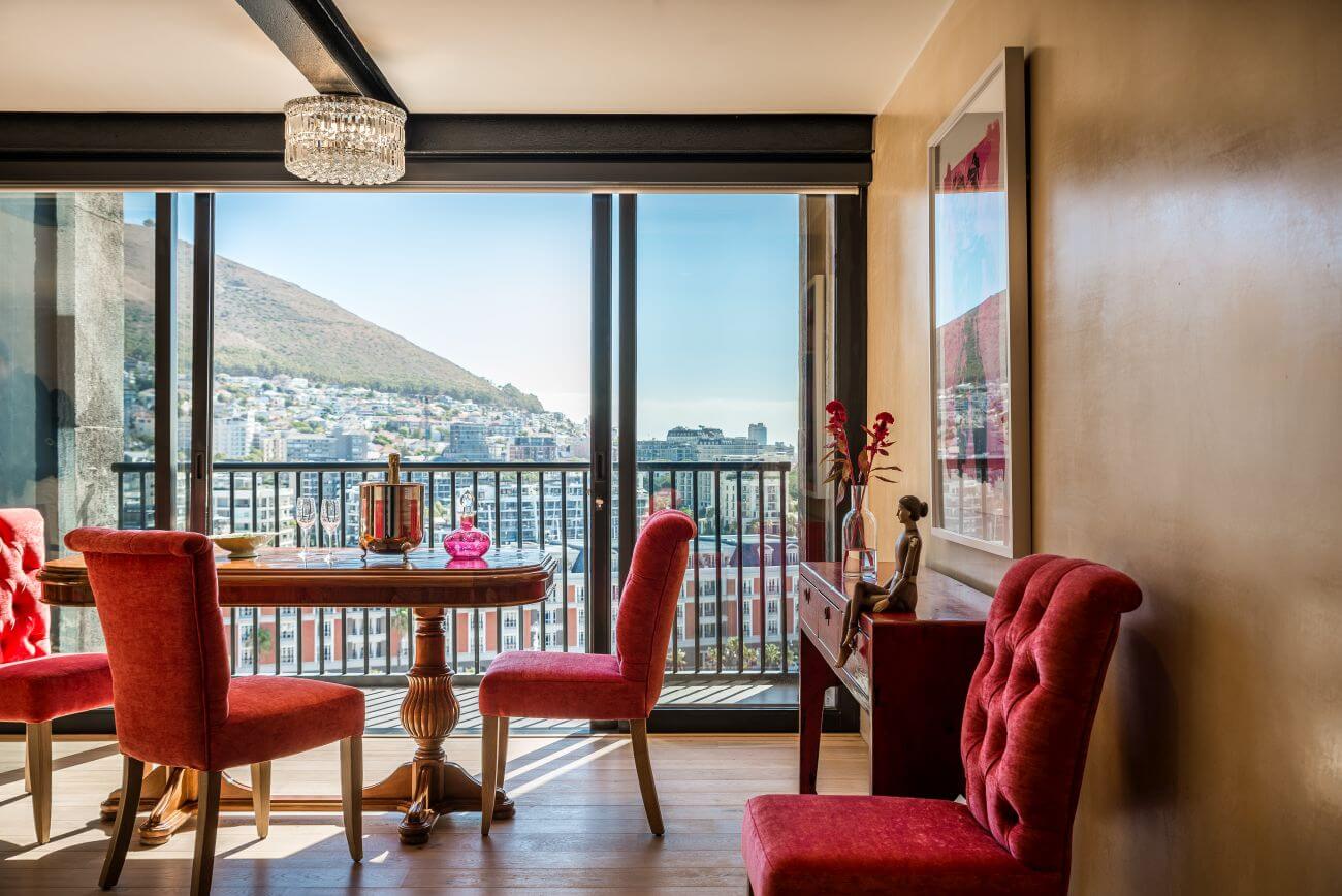 Esstisch mit roten Stühlen in einer Suite mit Aussicht auf Kapstadt.