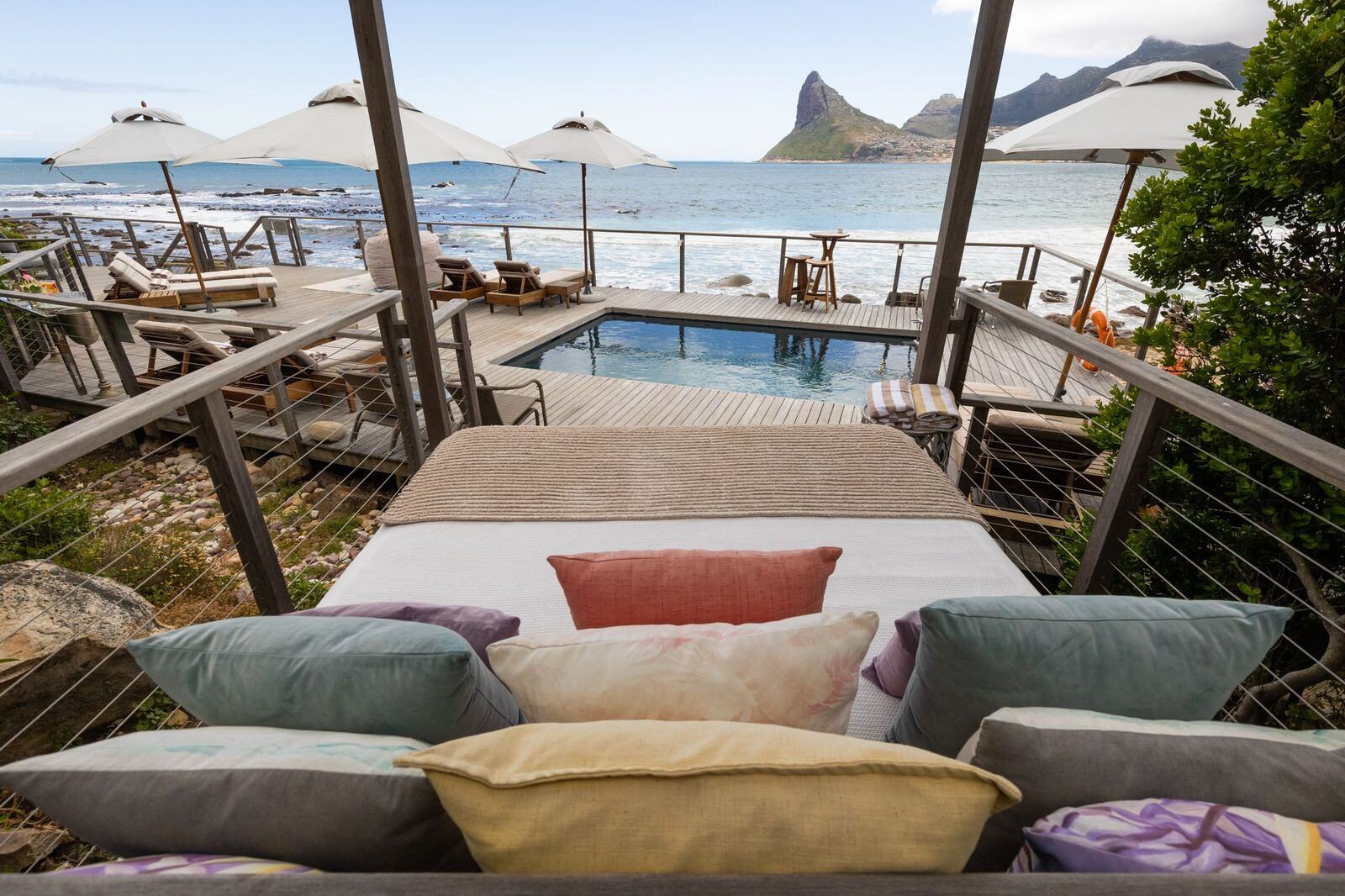Eine Matratze mit vielen Kissen liegt an einem Pool und hat gleichzeitig Sicht auf das Meer.