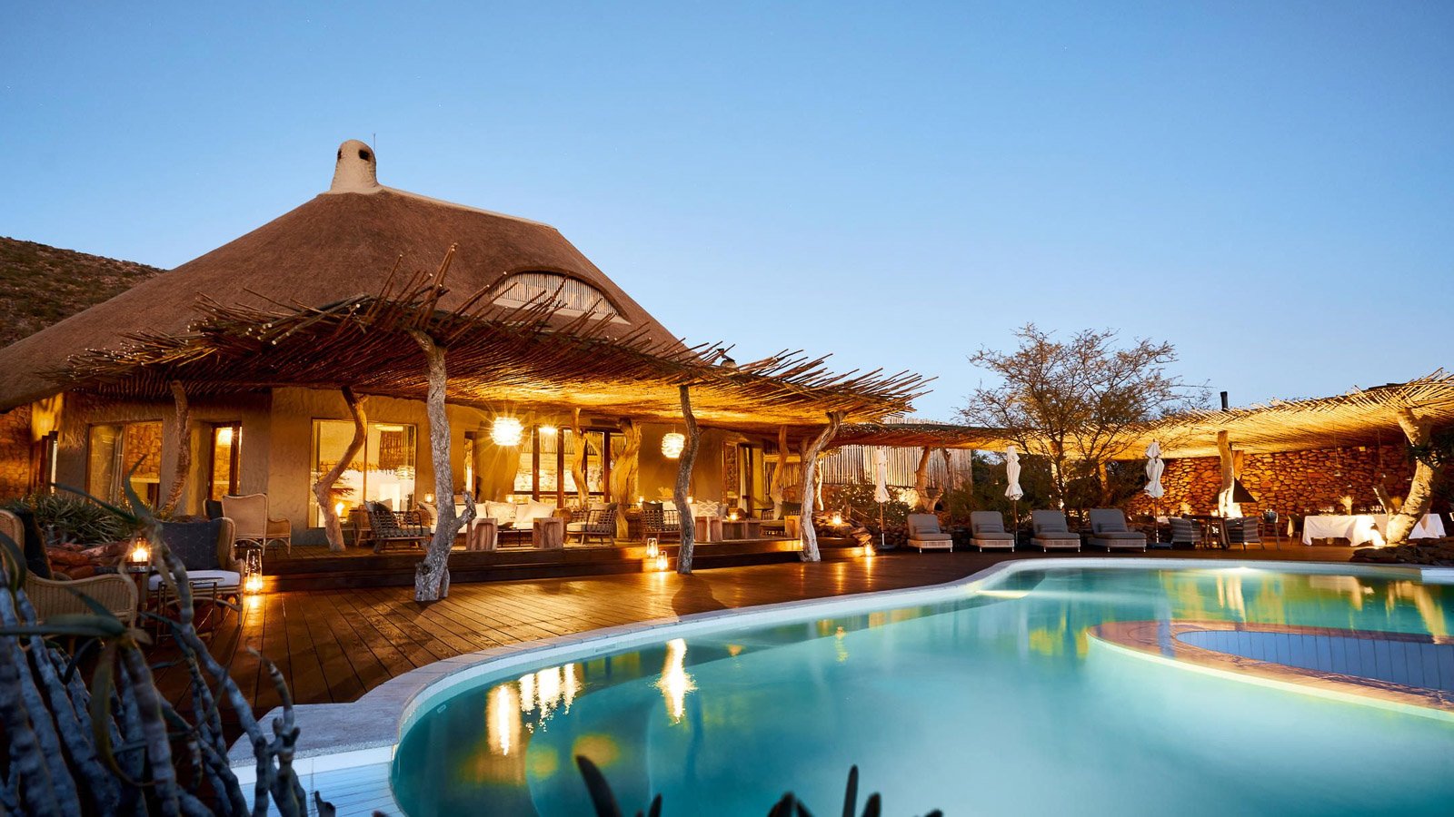 Pool mit beleuchteter Lodge im Hintergrund während der Abenddämmerung.