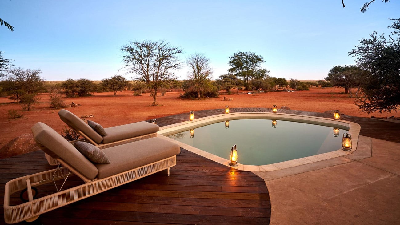 Privater Pool mit zwei Sonnenliegen, dahinter erstreckt sich die Kalahari.