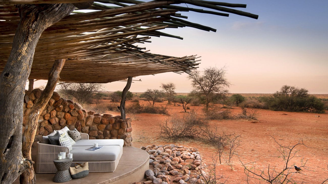 Ein Bett steht auf einer überdachten Plattform mit Blick in die rote Wüste der Kalahari.