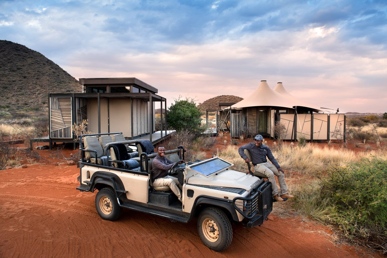 Zwei Guide sitzen in einem Safarijeep: einer am Lenkrad, einer auf dem Spooter-Sitz.