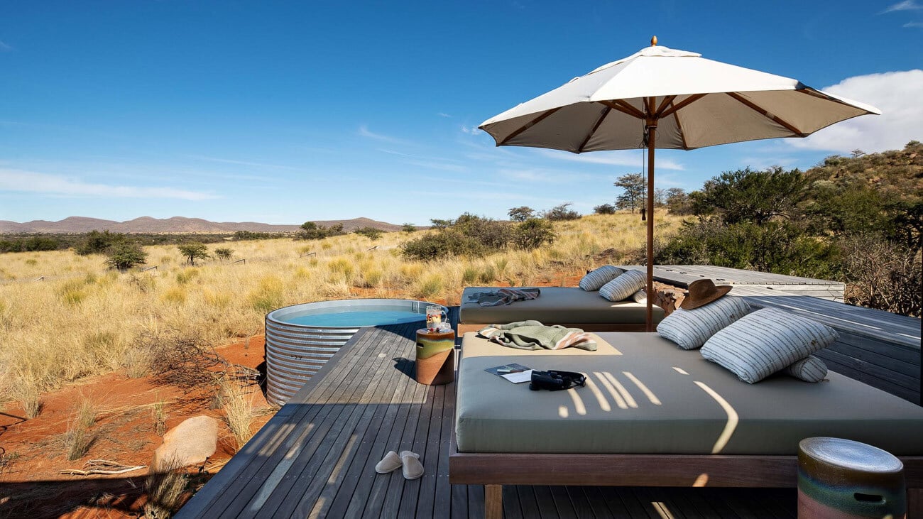 Sonnendeck mit Liegen und Sonnenschirm, im Hintergrund ist die Kalahari zu sehen.
