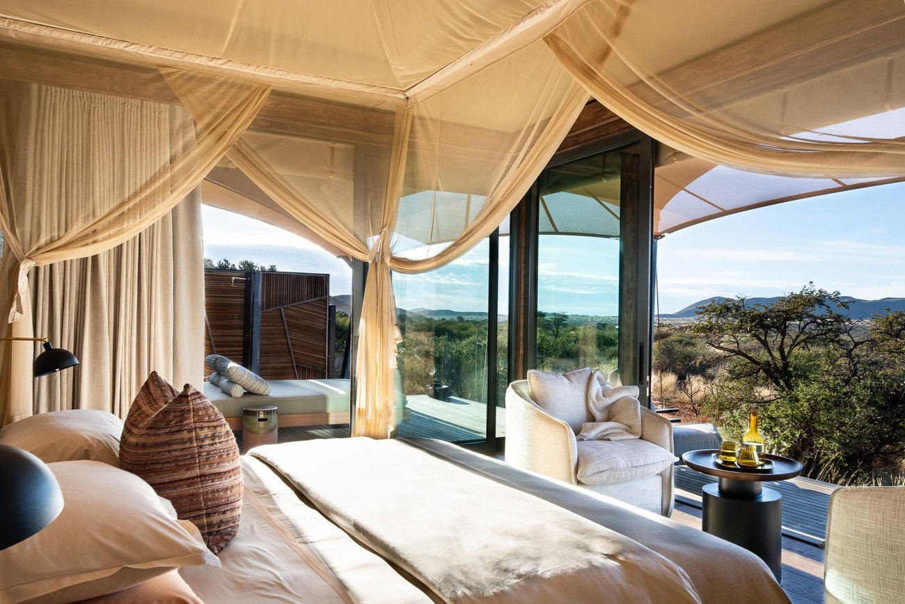 Kingsize-Bett mit Vorhängen von dem aus man einen freien Blick in die Natur hat.