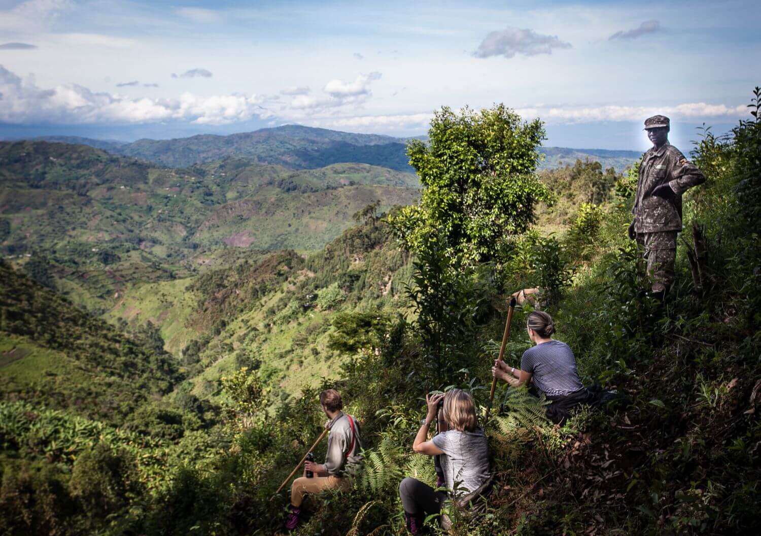 Drei Touristen machen mit einem Guide eine Wanderung durch die Berge Ugandas.