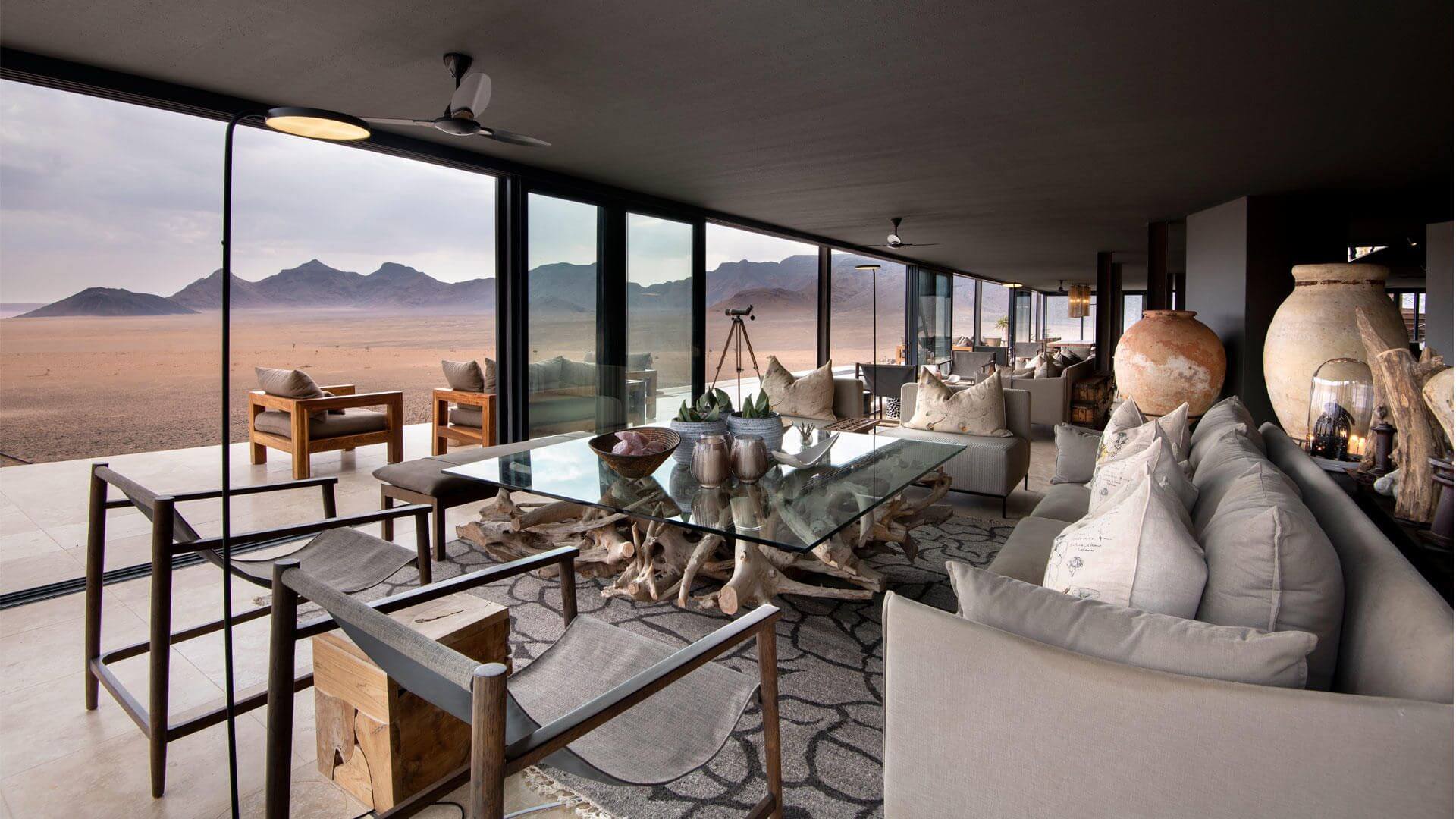 Cremefarbene Einrichtung einer Lodge. Es gibt raumhohe Fenster, die einen freien Blick auf die Wüstenlandschaft ermöglichen.
