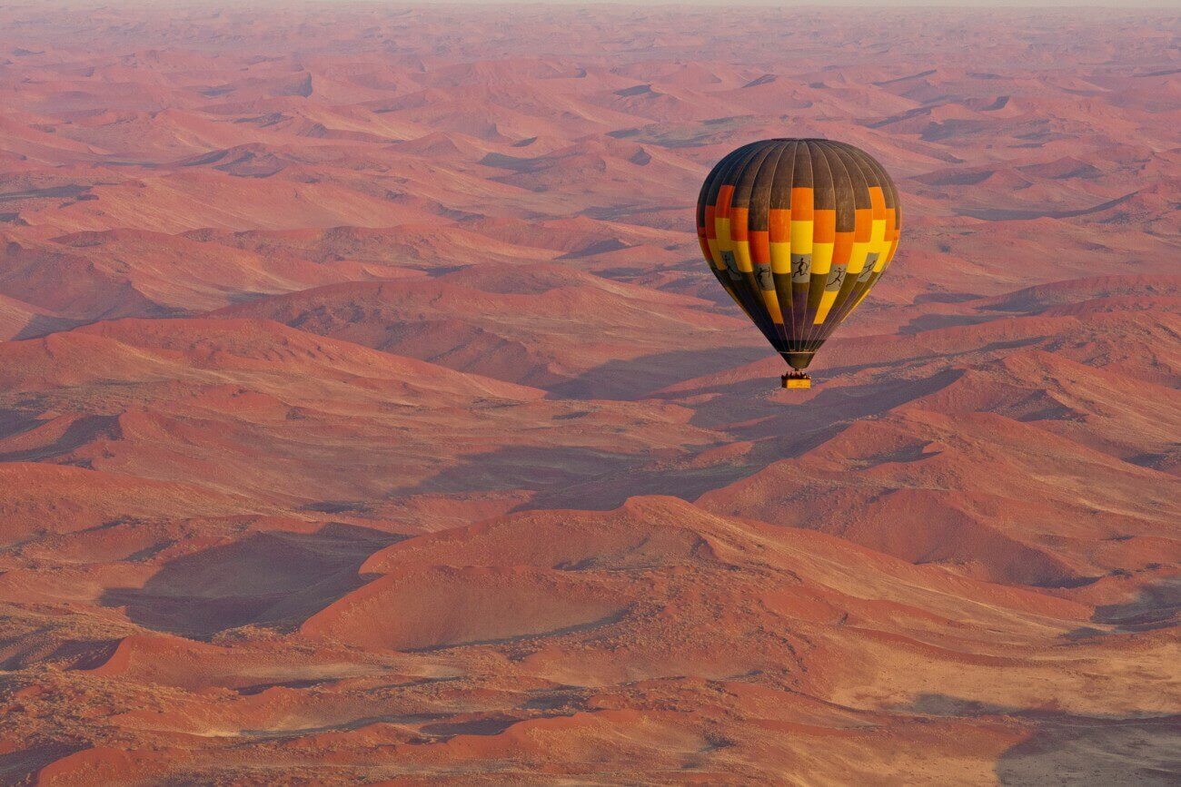 Ein bunter Heißluftballon fährt über die roten Dünen Namibias.