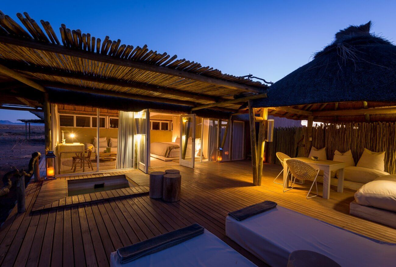Beleuchtete Lodge mit Terrasse und Sonnenliegen in der Dämmerung.