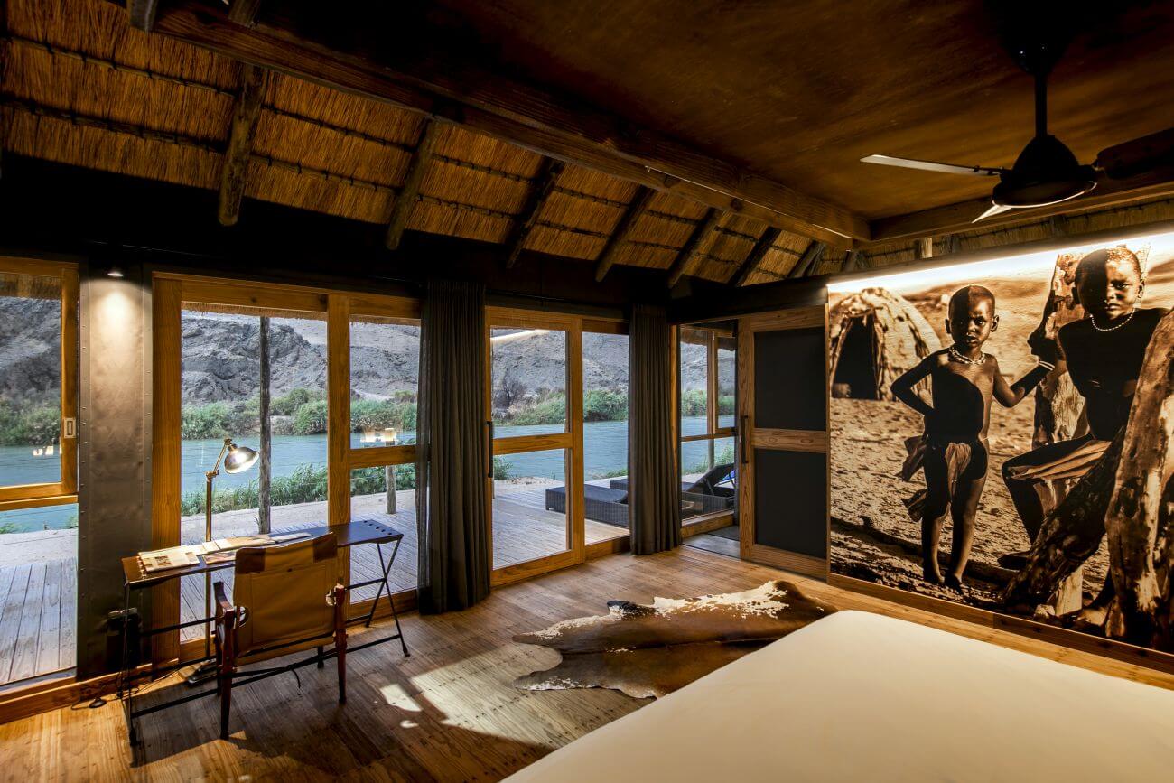 Blick von einer Lodge auf den angrenzenden Fluss. An der Wand hängt außerdem ein beeindruckendes Bild von drei Kindern aus Namibia.