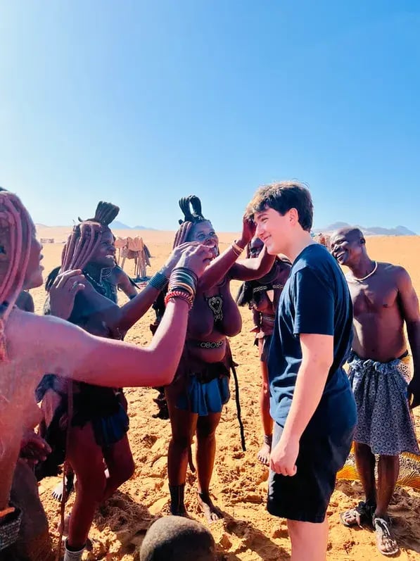 Himba-Frauen befühlen die Haare eines weißen Jungen, der zu Besuch ist.