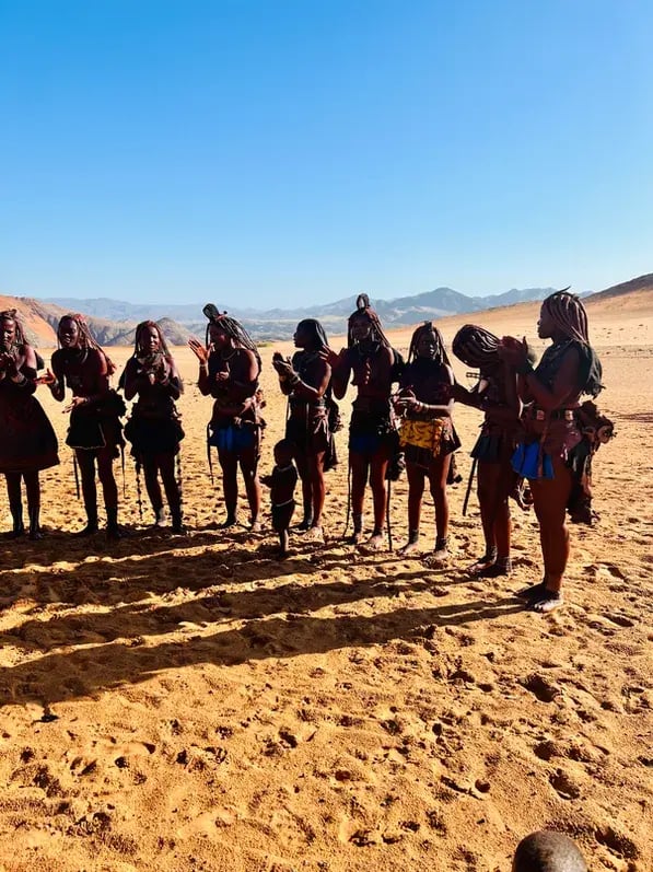 Himba-Frauen in Namibia stehen in einer Reihe nebeneinander, bereit für einen Tanz.