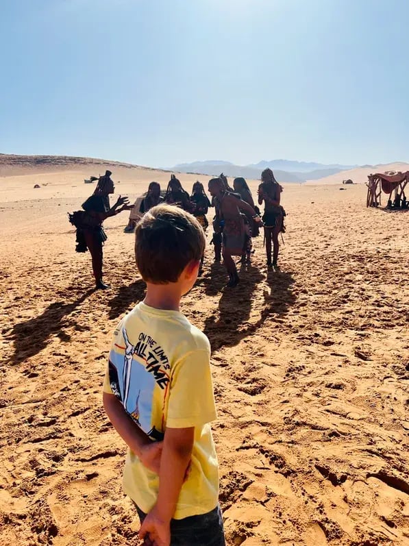 Ein kleiner Junge steht bei einem Besuch vor einer Gruppe Himba-Frauen in Namibia.