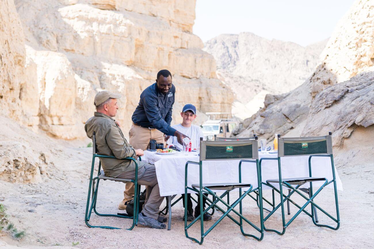 Zwei Touristen sitzen an einem Tisch an einer Felswand und werden bedient.
