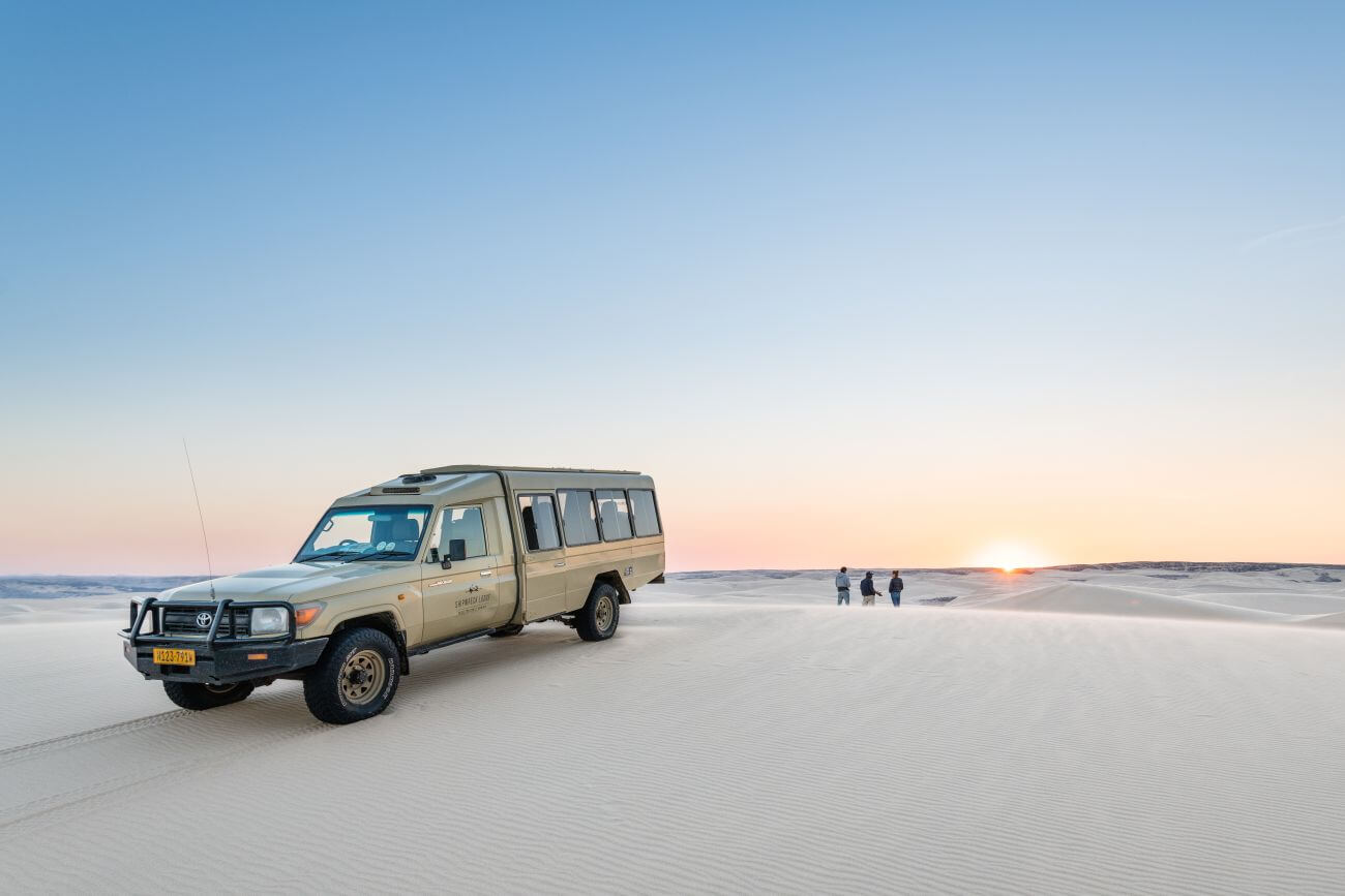 Ein Jeep steht einer endlosen flachen Wüste bei Sonnenaufgang.